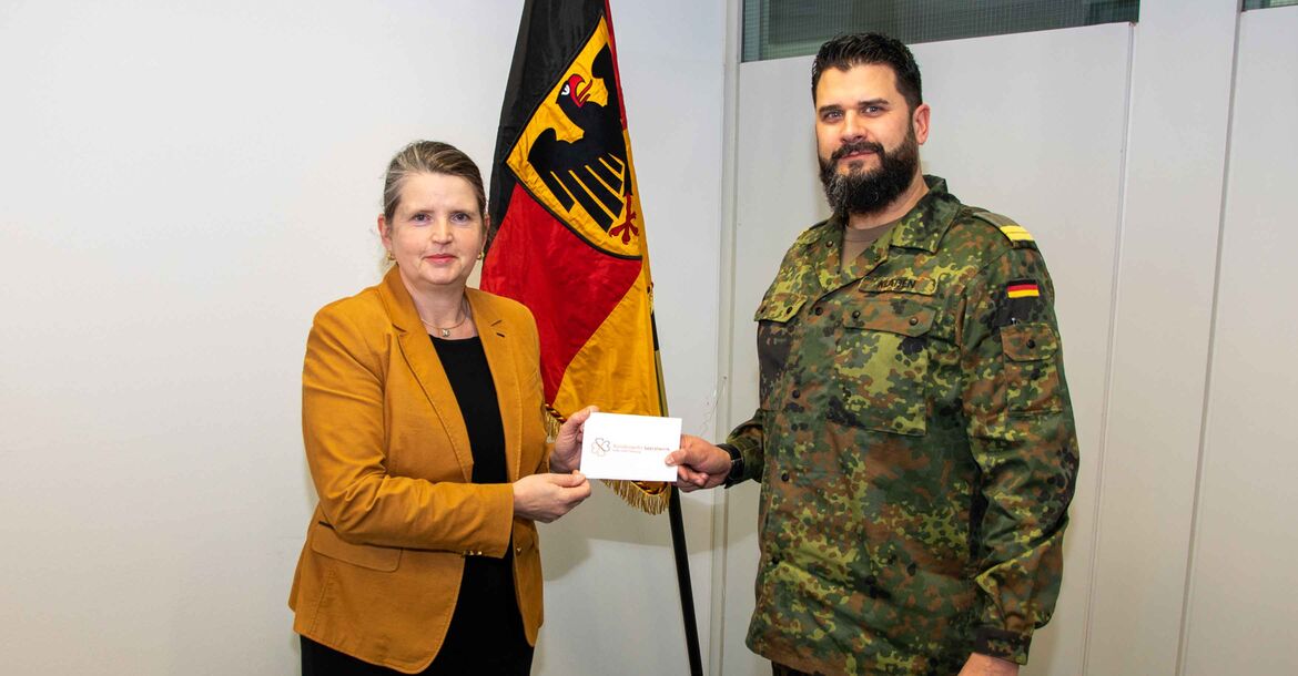 Oberleutnant zur See Dennis Klaßen übergibt den Briefumschlag mit der Spendensumme an Oberregierungsrätin Marion Gerber. 
