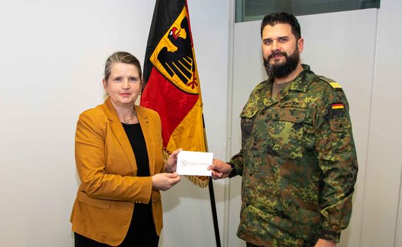 Oberleutnant zur See Dennis Klaßen übergibt den Briefumschlag mit der Spendensumme an Oberregierungsrätin Marion Gerber. 